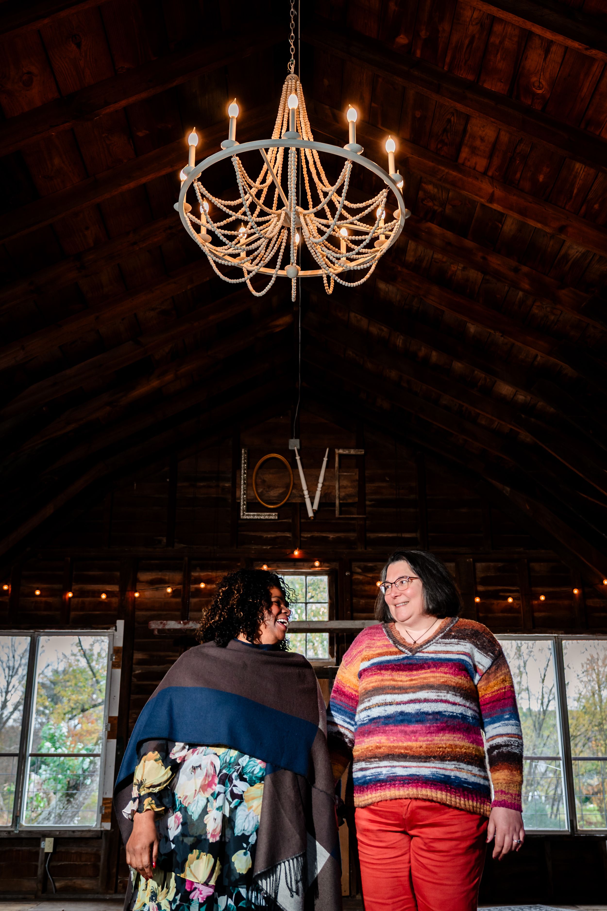 Rustic barn interior with elegant chandeliers and large windows creates a romantic wedding venue atmosphere.