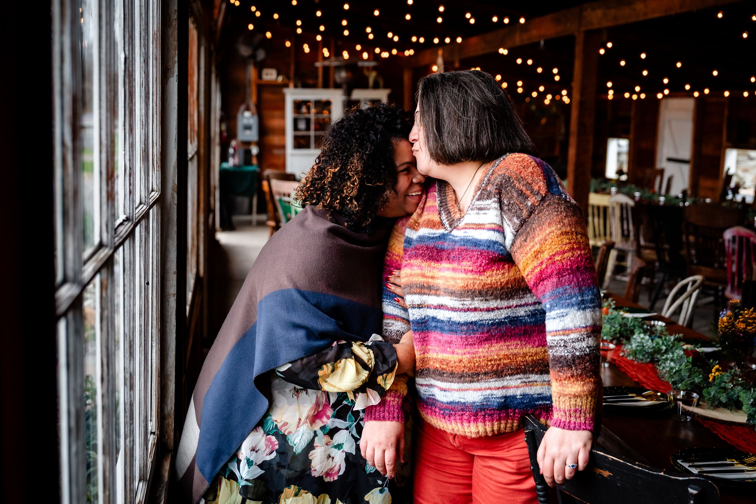 People enjoy a cozy indoor gathering with string lights and rustic decor in a barn-like setting.