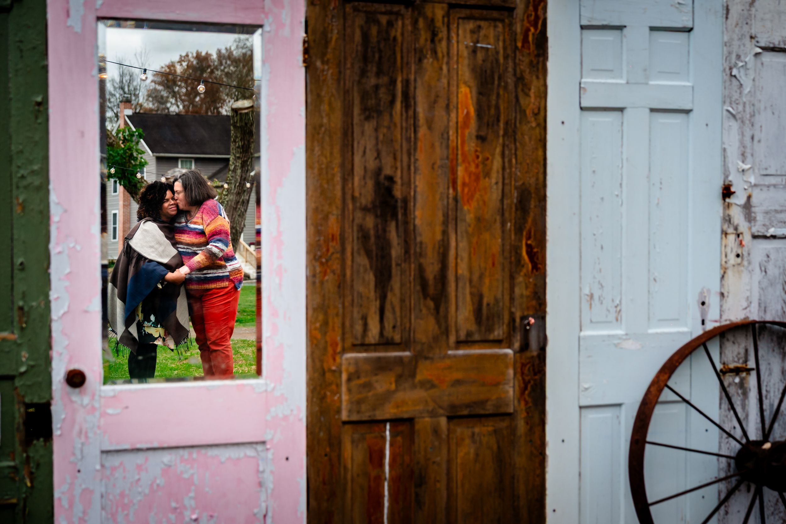 A rustic wooden door with peeling paint stands between pink walls with window openings.
