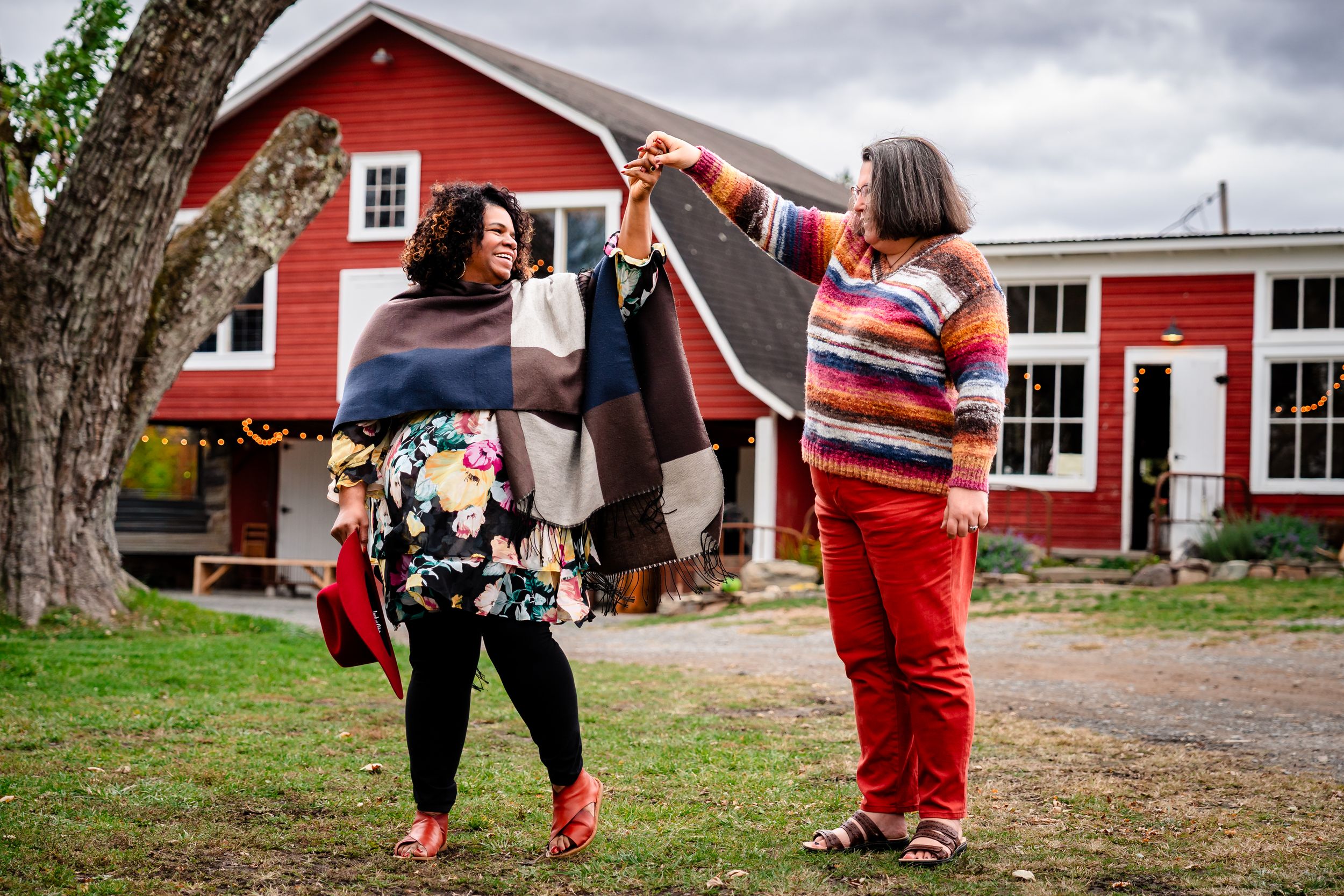 Family plays together outside a red barn on an overcast autumn day.