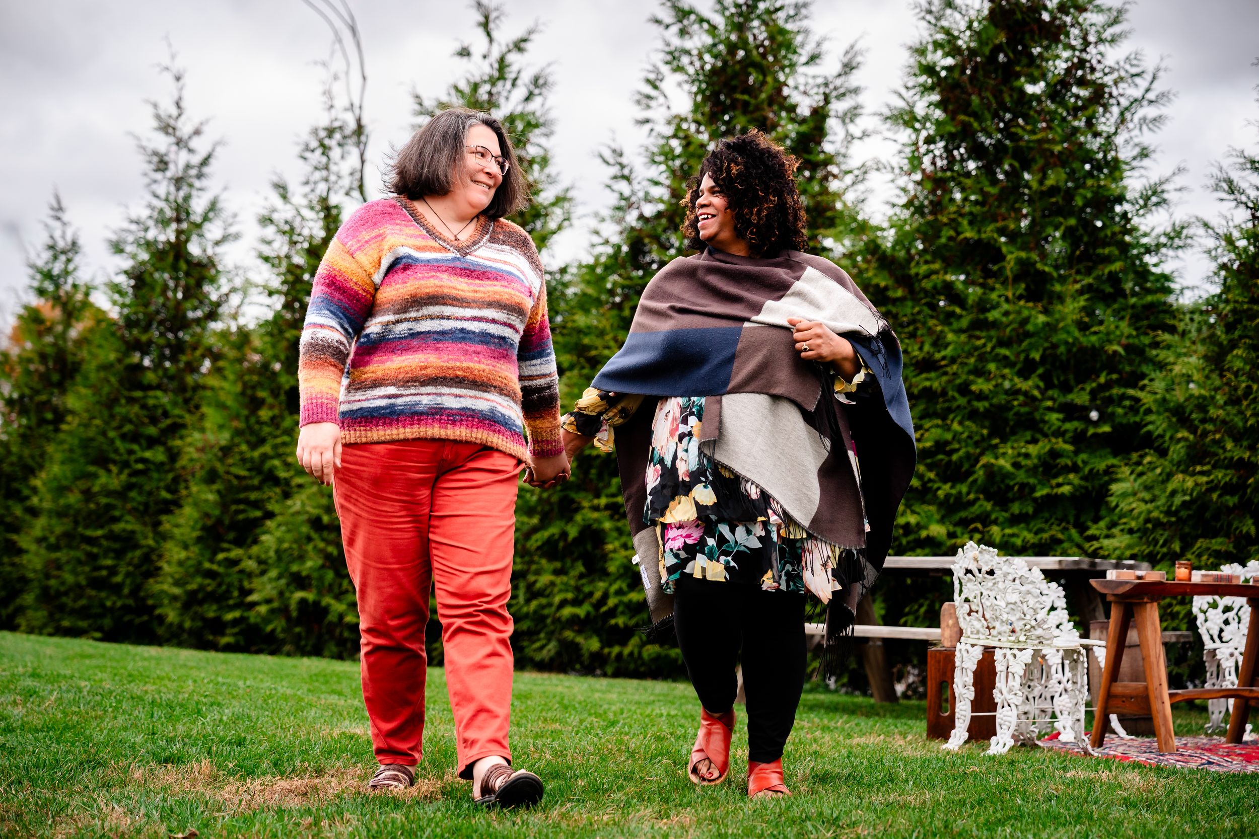 People enjoying a sunny day outdoors with evergreen trees in the background while sitting on grass.