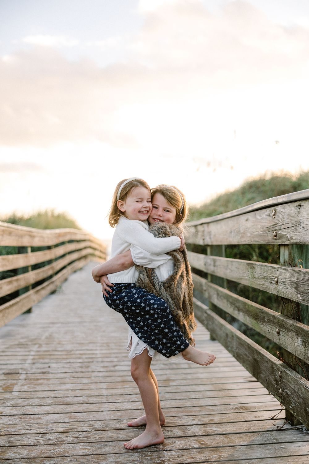 Young child in a polka dot dress plays and dances on a wooden boardwalk during golden hour.
