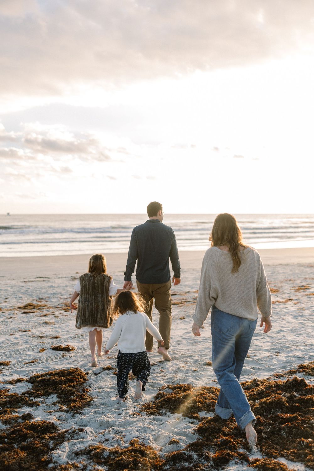 Family walks together along a beach with seaweed at sunset, viewed from behind.