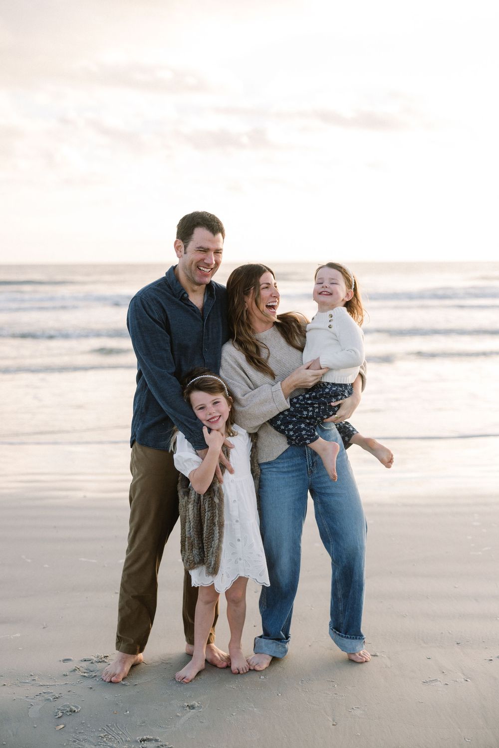 Family enjoying a playful moment together on a sunny beach during golden hour.