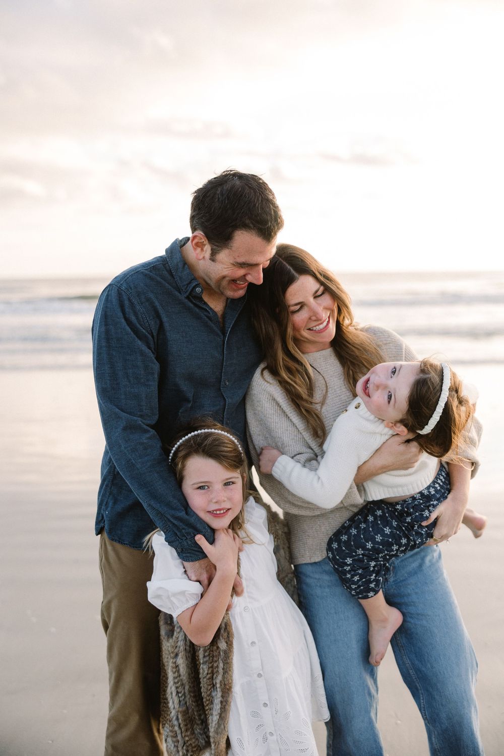 Candid family portrait showing joyful laughter and embraces on the beach at sunset.