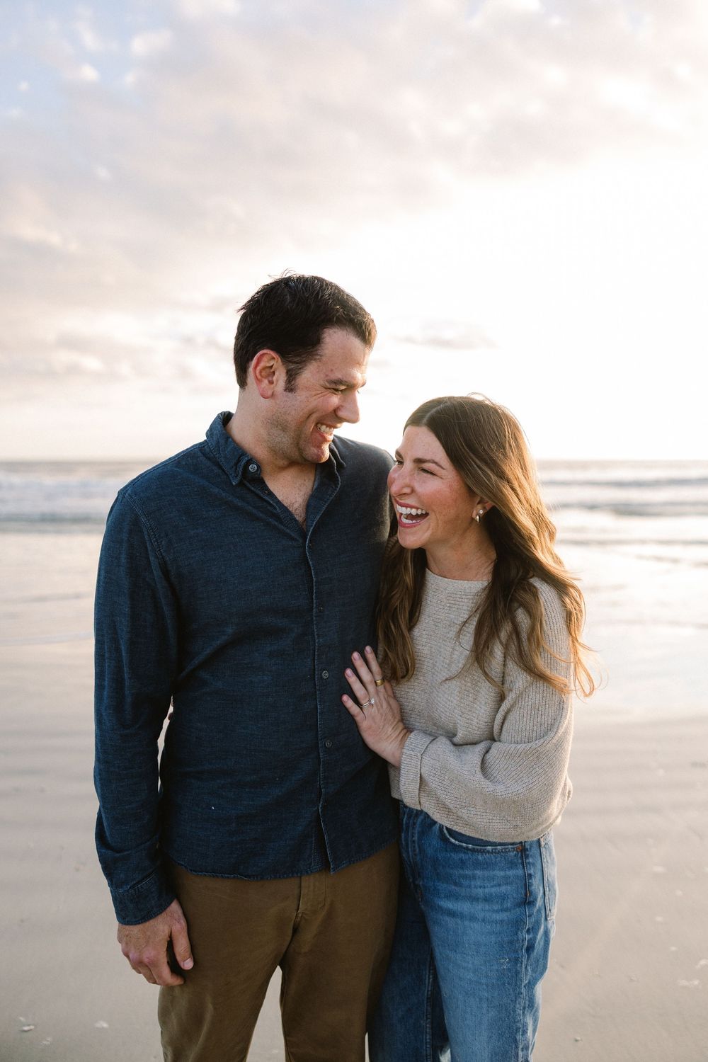Couple sharing intimate laughs while walking along a misty beach shoreline.