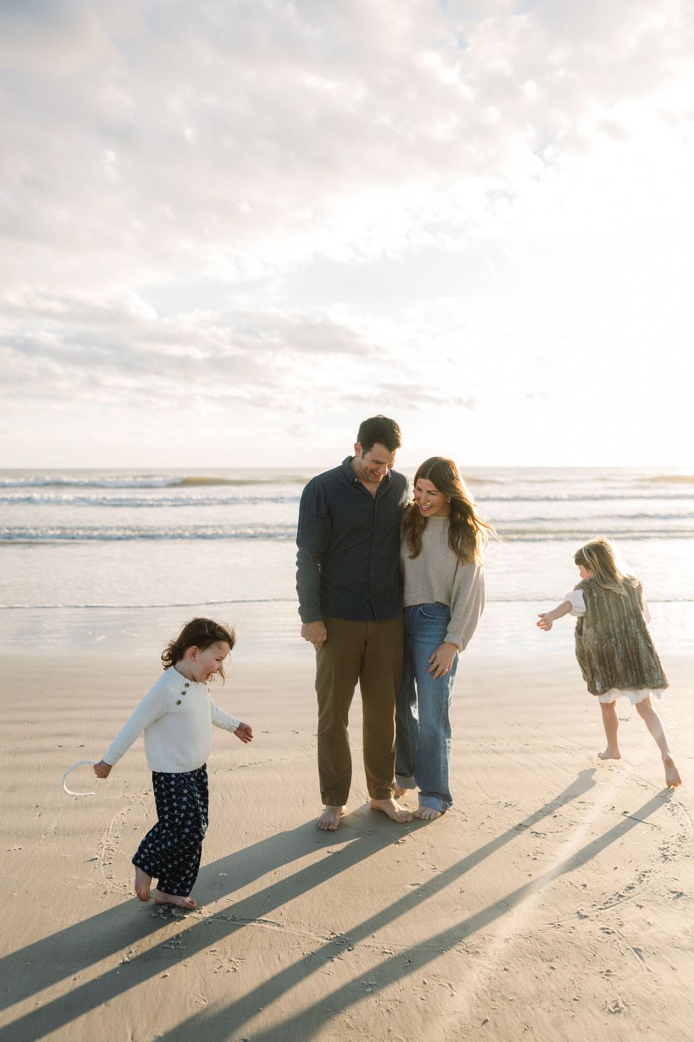 Family walking along a sunny beach casting long shadows in the sand during golden hour.