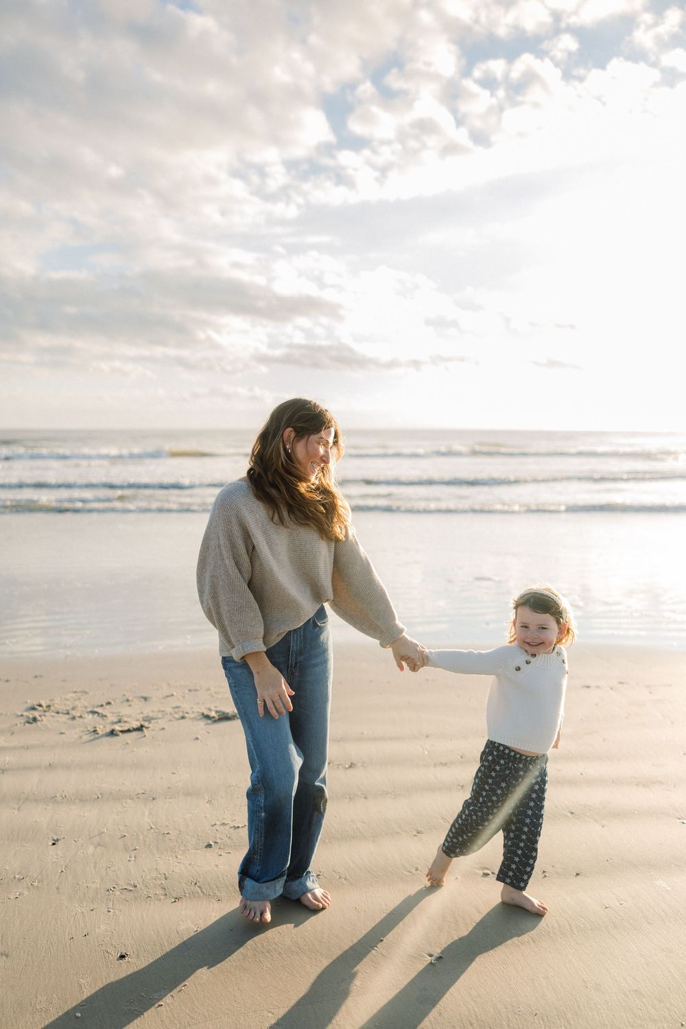 Parent and child playing together on sandy beach with long shadows at sunset.
