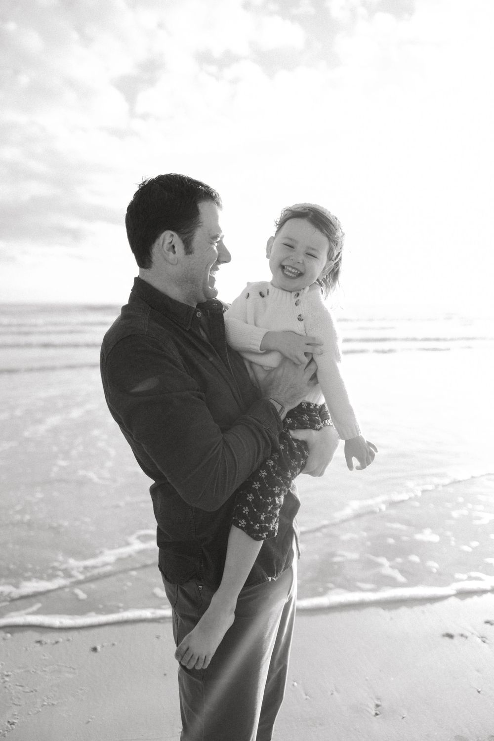 A playful moment captured between parent and child at the beach in black and white photography.