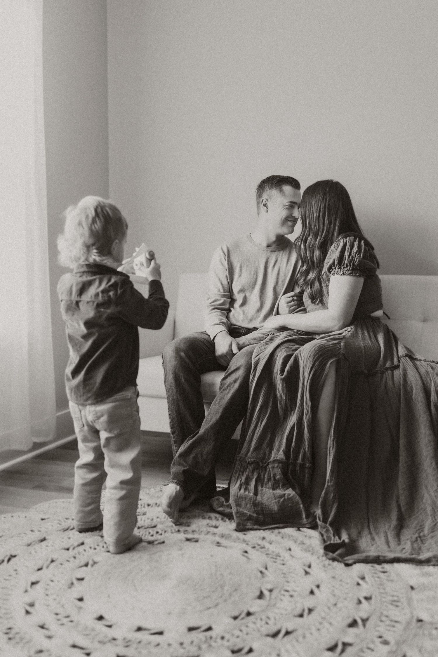 Toddler boy standing and pretending to take a photo of his parents on the couch during a Maryville, TN studio session