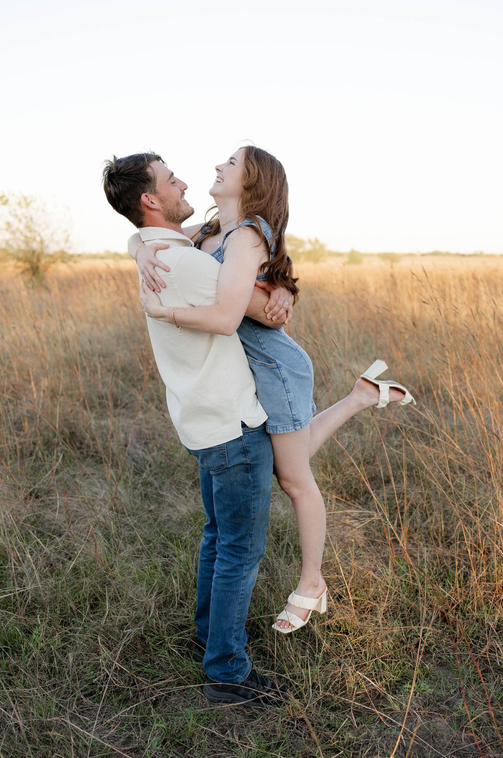 True West Photography - Playful couple laughs and embraces in golden field during sunset photoshoot.