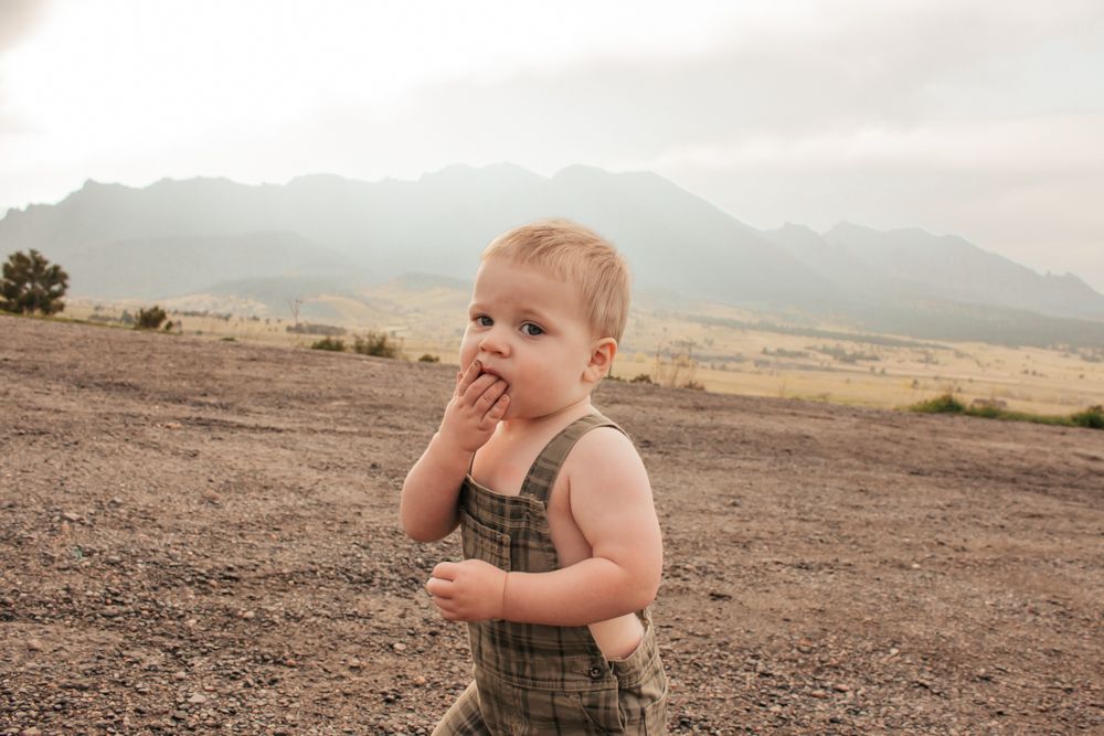 Toddler in overalls eating a snack outdoors with mountain landscape in the background | Westminster Family Photographer