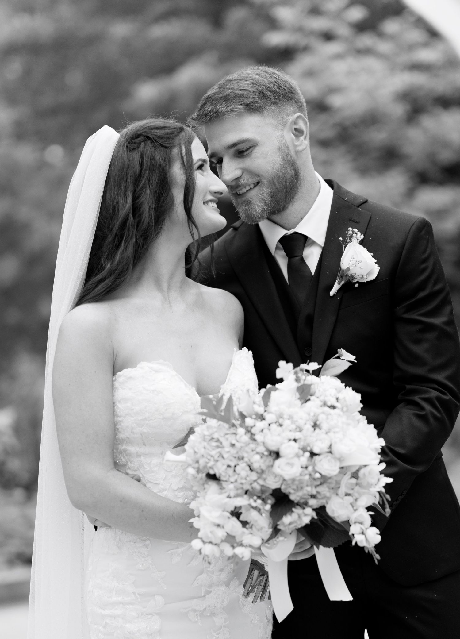 Black and white portrait of newlyweds sharing an intimate moment with floral bouquet.