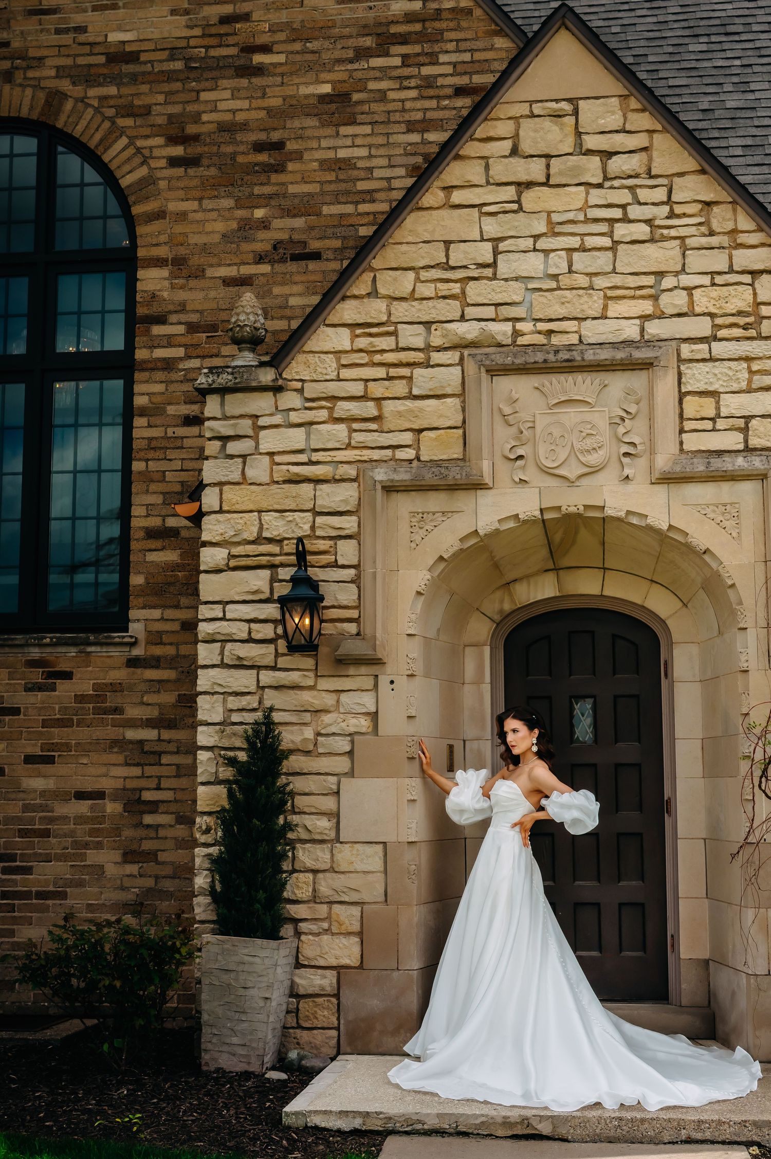 Elegant white wedding gown with dramatic puff sleeves photographed against stone church entrance with arched doorway.