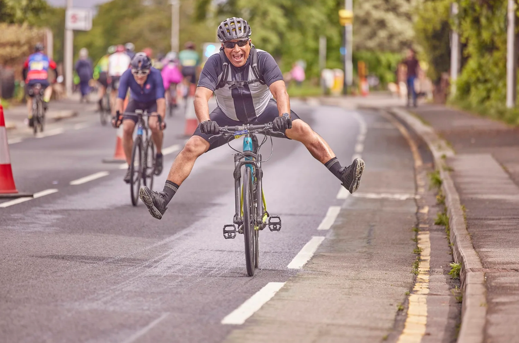 Cyclist performs playful stunt by spreading legs while riding on city street during group bike ride.