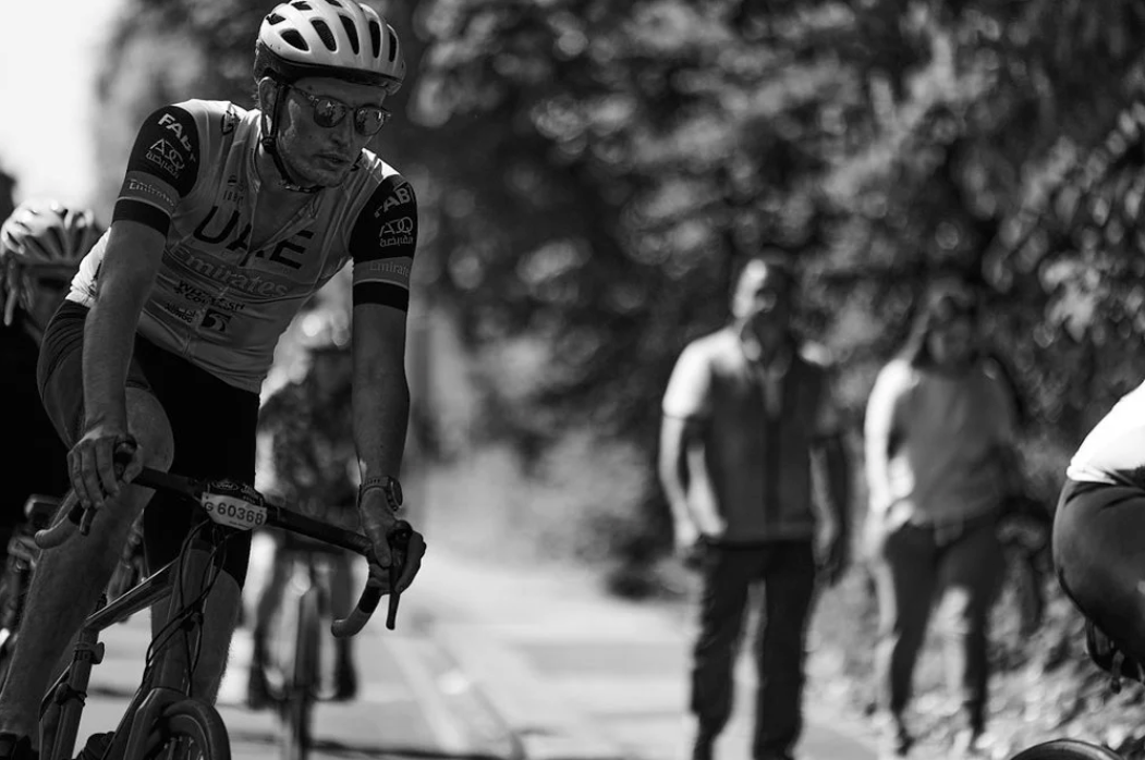 Cyclists ride in a pack along a tree-lined road during a competitive cycling race in black and white.