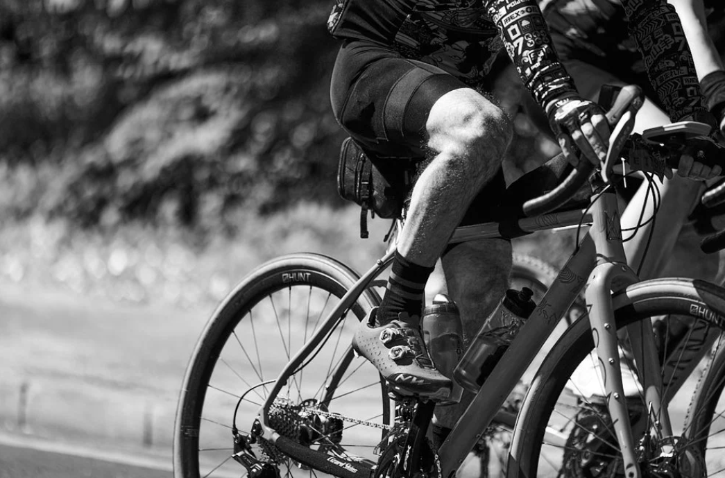 Black and white close-up of cyclist legs pedaling on a road bike during competition.