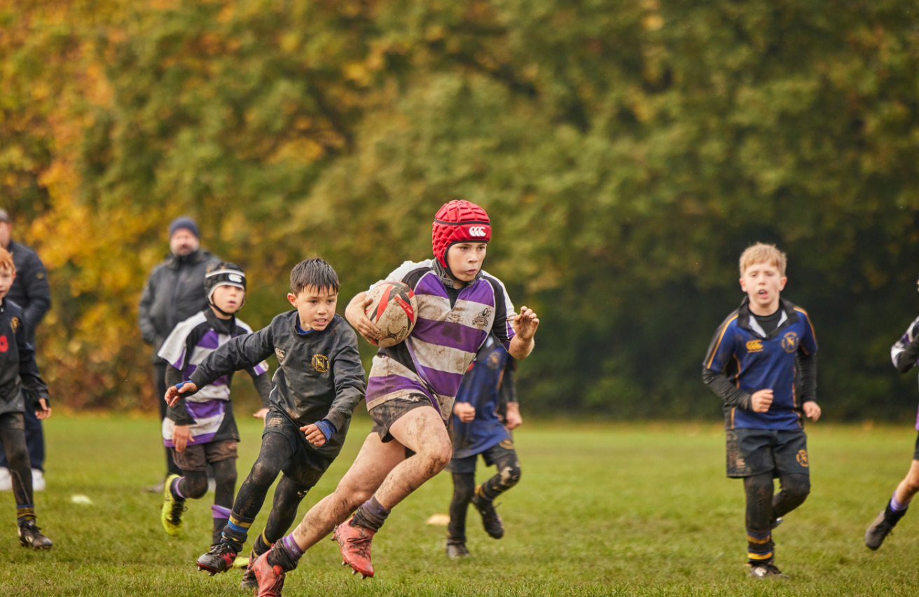 Youth rugby players engaged in a dynamic match on an autumn field with colorful trees in the background.