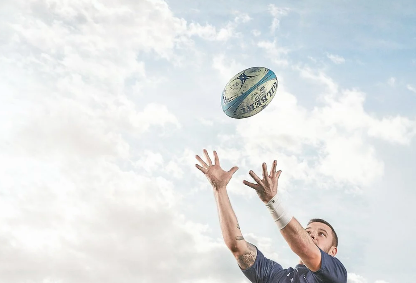 Rugby players practicing ball catching drills against cloudy sky background.