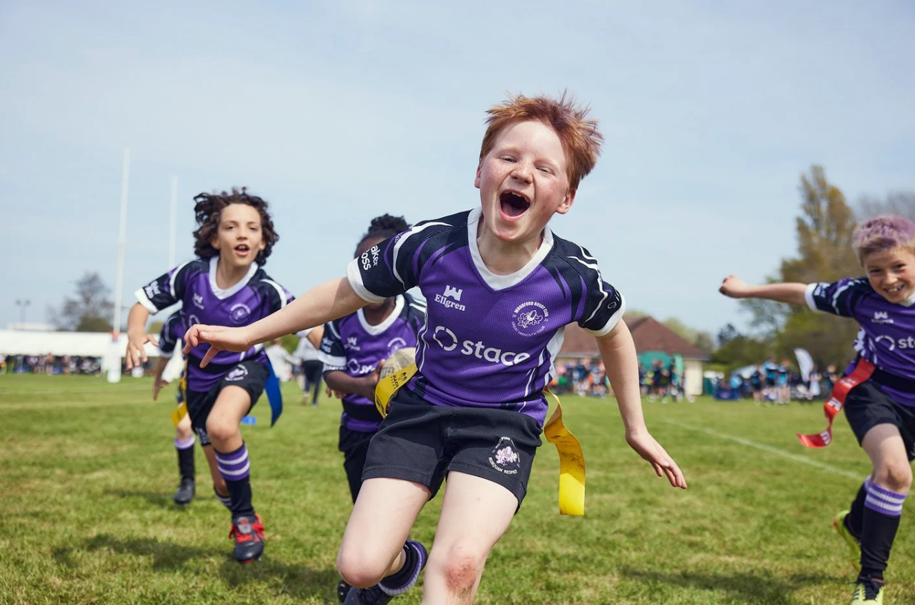 Youth rugby players in purple uniforms run and celebrate during an exciting match.