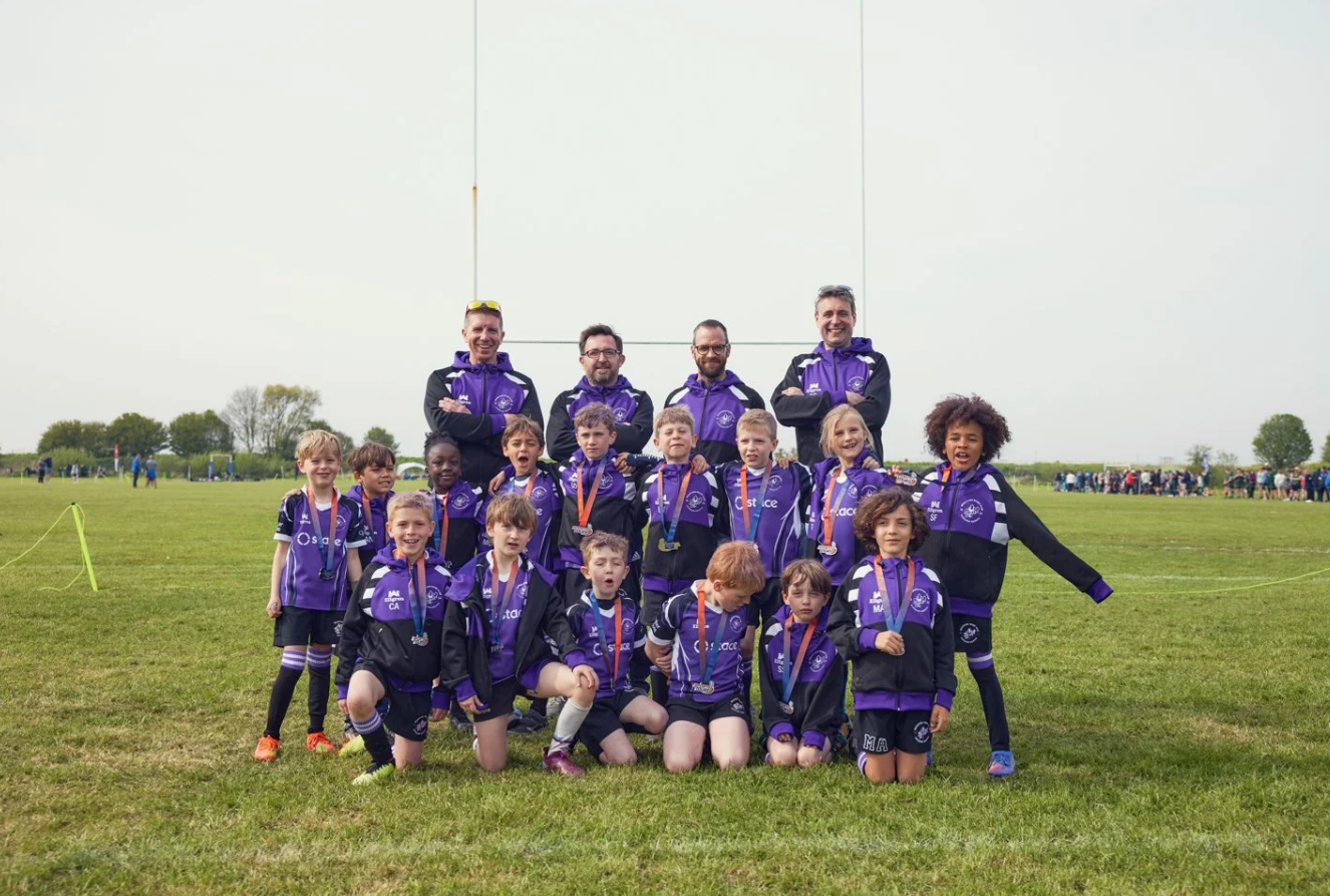 Youth rugby team in purple jerseys poses together on the field for a group photo.