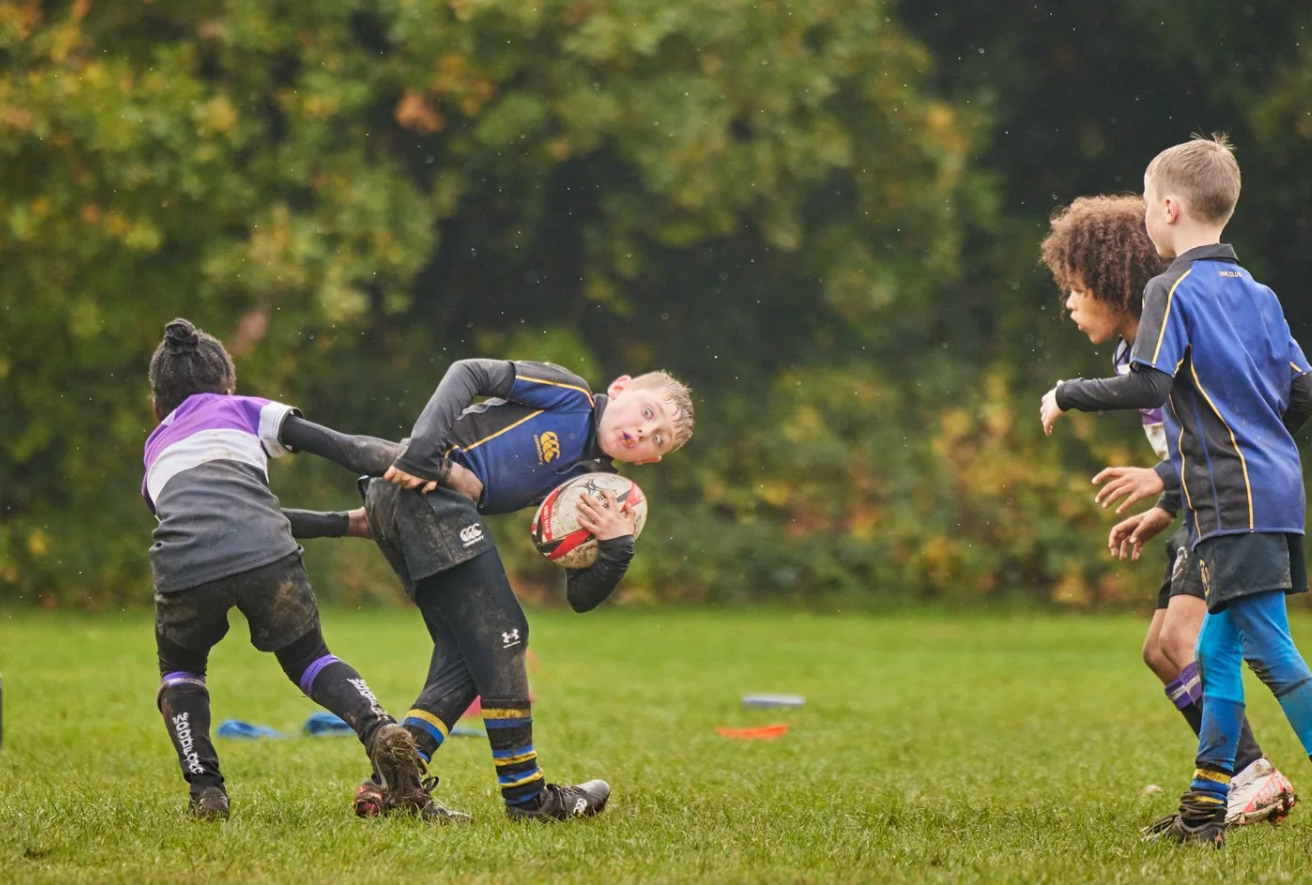 Young rugby players dive and tumble during an energetic practice session on a grass field.