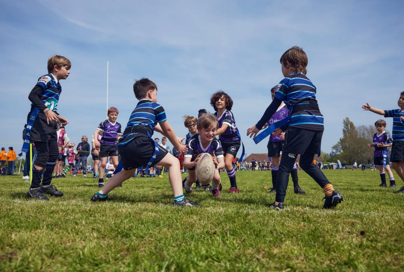 Young soccer players sitting on a grassy hill during a break at a sports field on a sunny day.