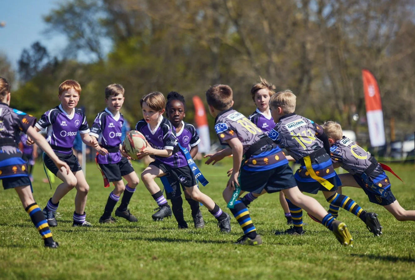 Rugby players perform synchronized push-ups during an outdoor training session on a sunny day.
