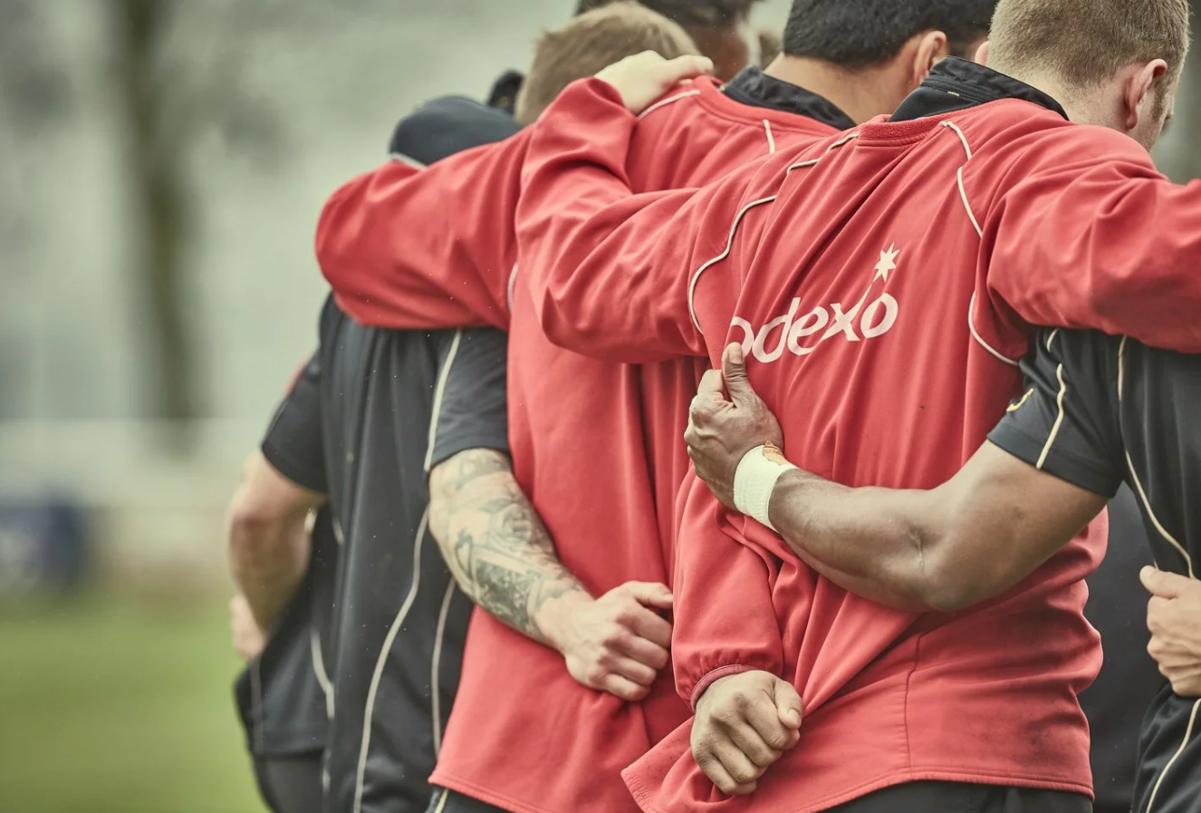 Soccer players in red and black uniforms huddle together during a training session on the field.