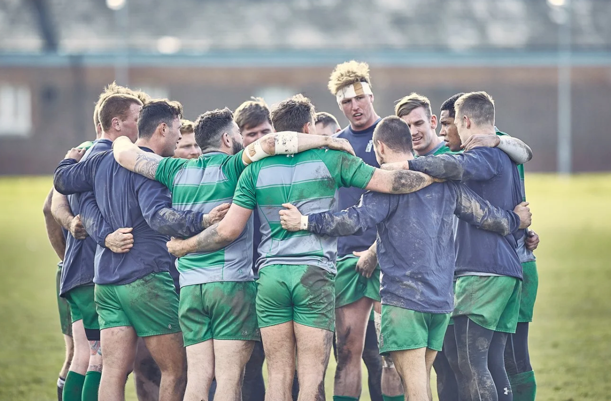 Rugby players in green jerseys huddle together on the field during a match.