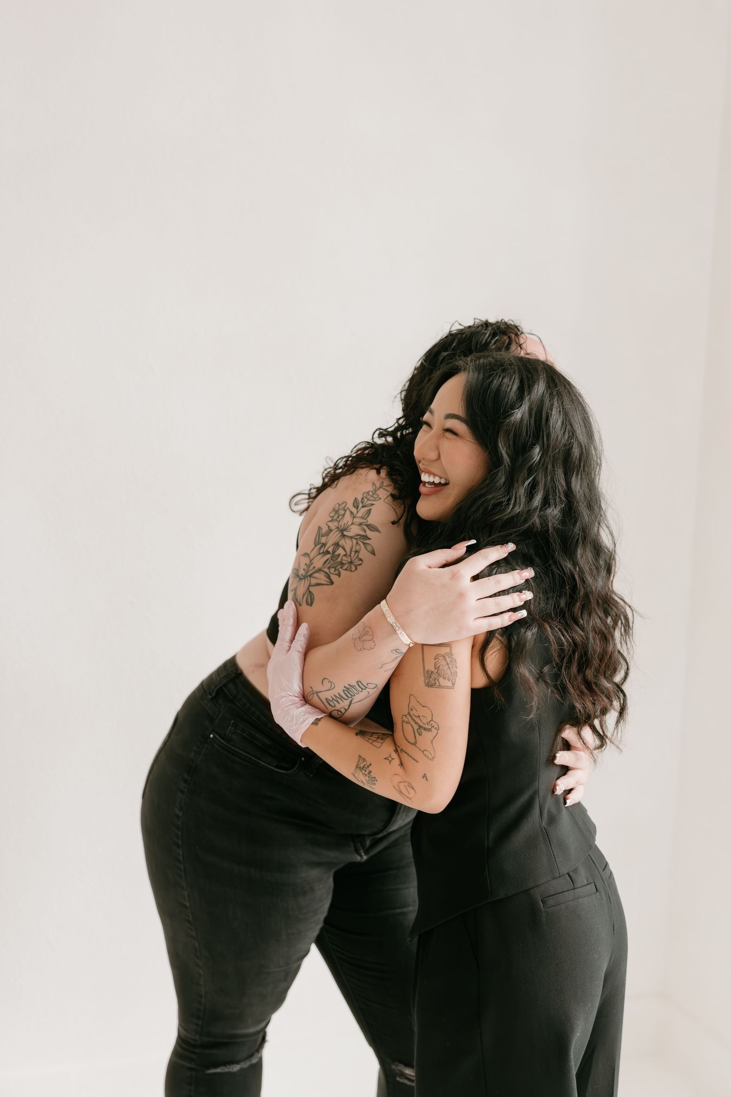 Two people in black outfits interact with each other while seated on modern chairs against a white backdrop.