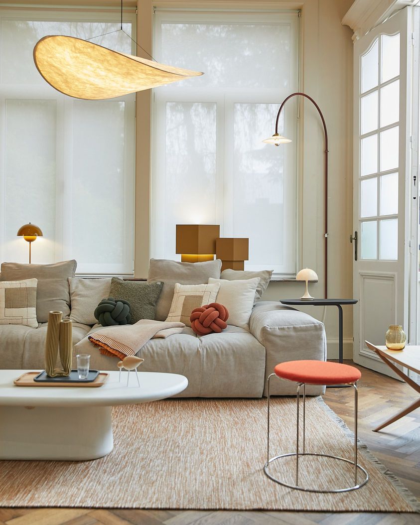 Modern living room interior with white sofa, round side table and paper lantern pendant light against bright windows.