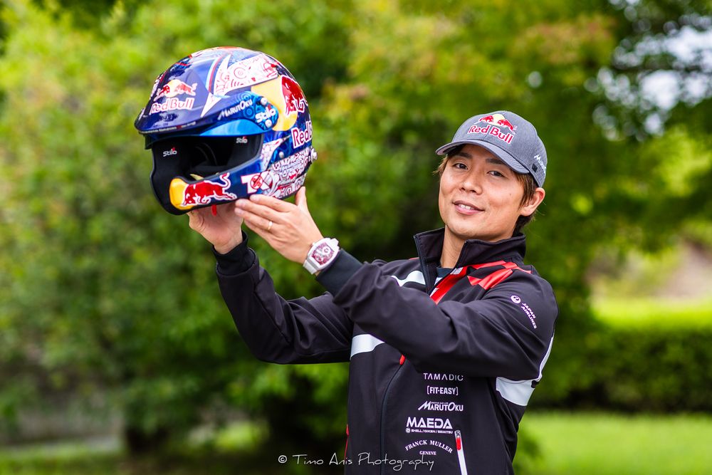 Racing driver celebrates victory by raising trophy during motorsport podium ceremony.