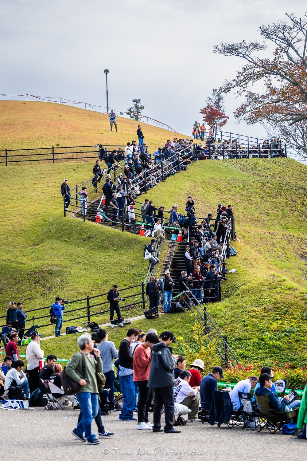 Crowd of spectators climbing outdoor stairs on a grassy hillside at a public viewing area or event venue.