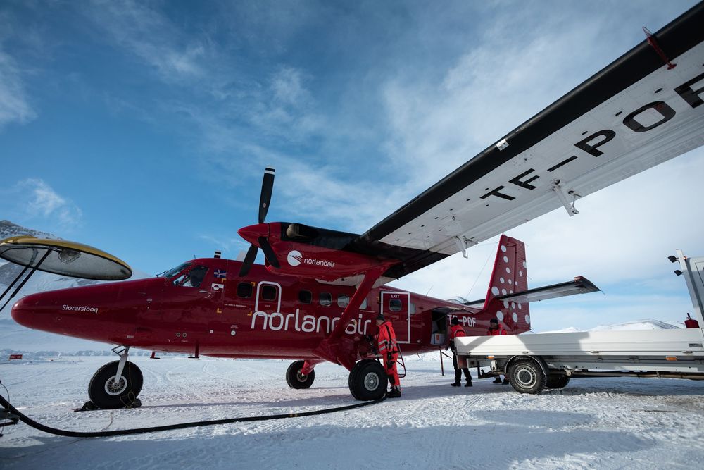 Red and white ski planes parked on snowy terrain against a bright blue sky at a remote winter airfield.