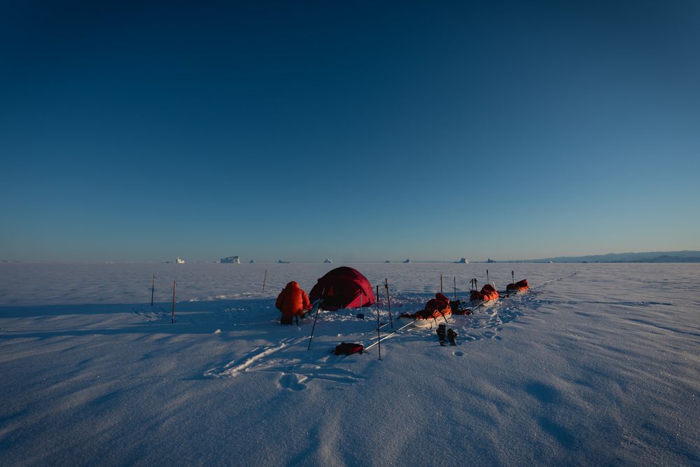 Expedition team travels across vast snowy Arctic landscape with sleds and equipment during polar expedition.
