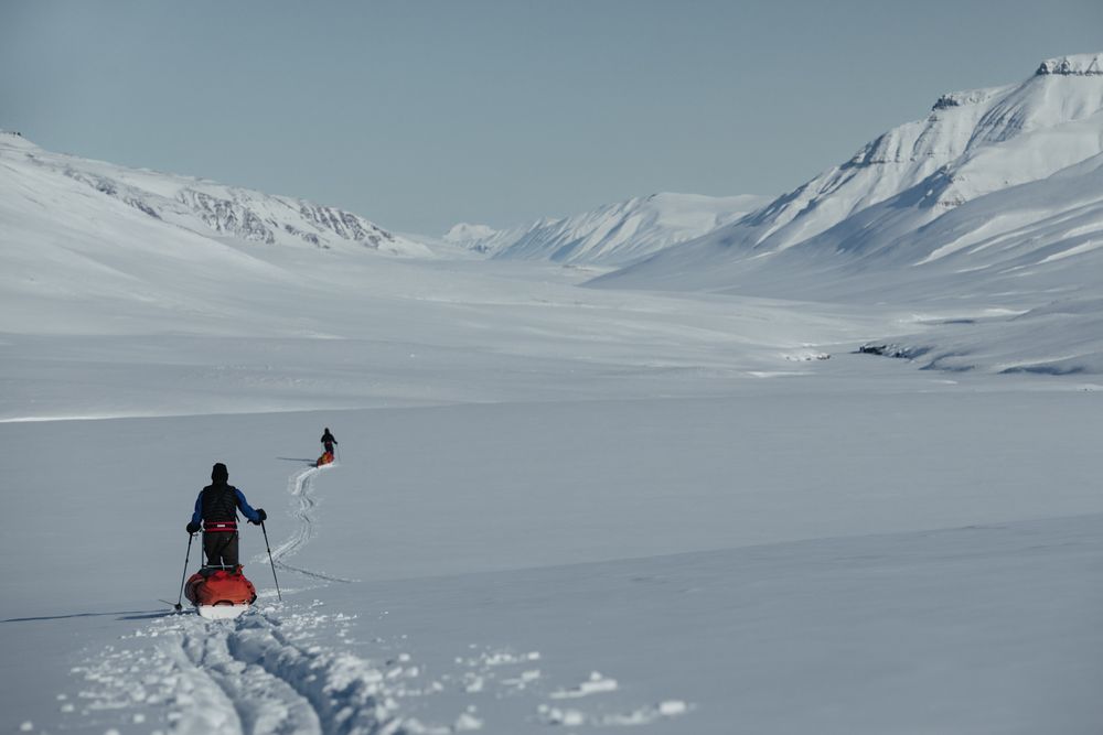 Two people skiing across a vast snowy landscape surrounded by snow-covered mountains in winter.