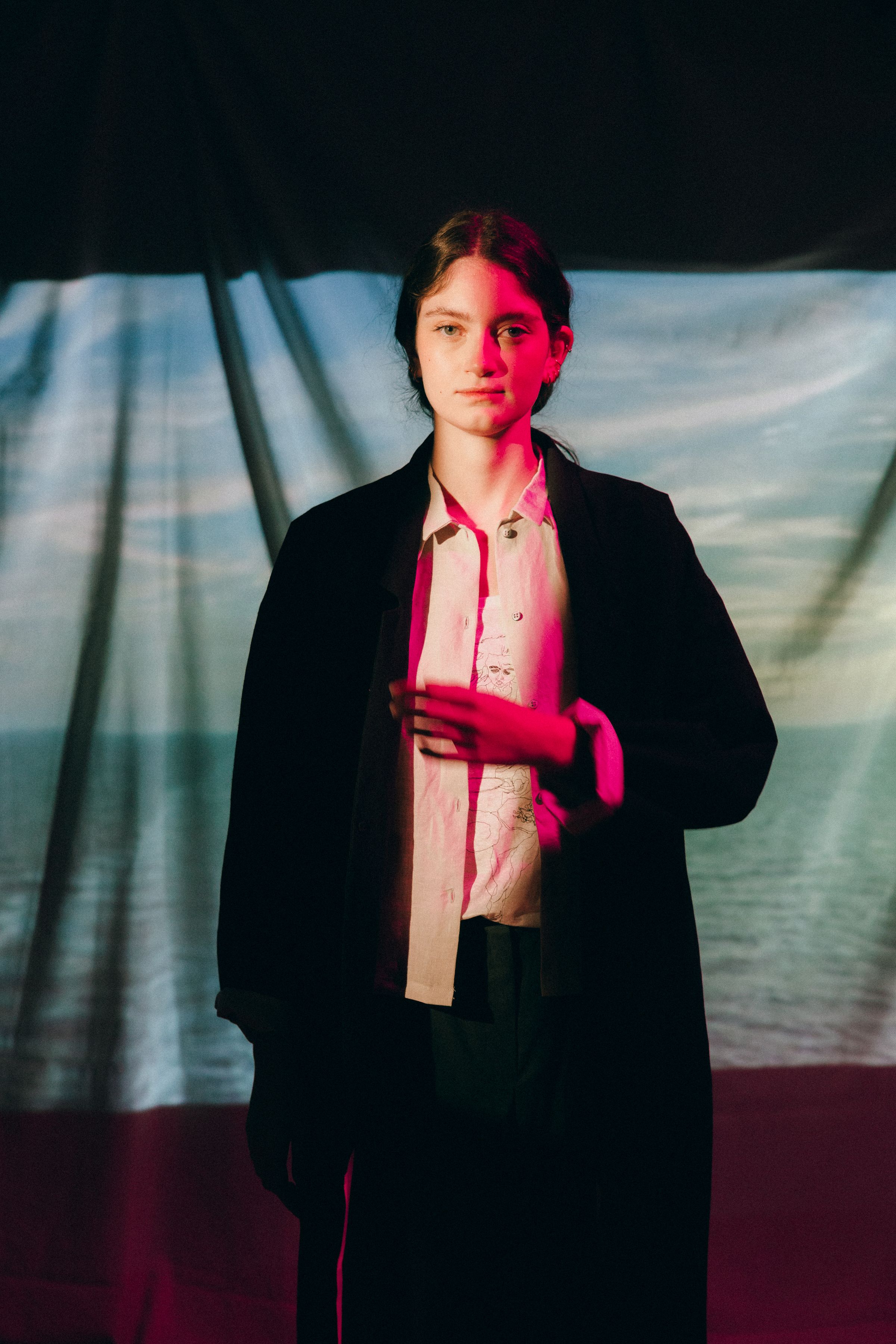 Dramatic portrait series in dark lighting with red tint showing figure in black coat against moody background.