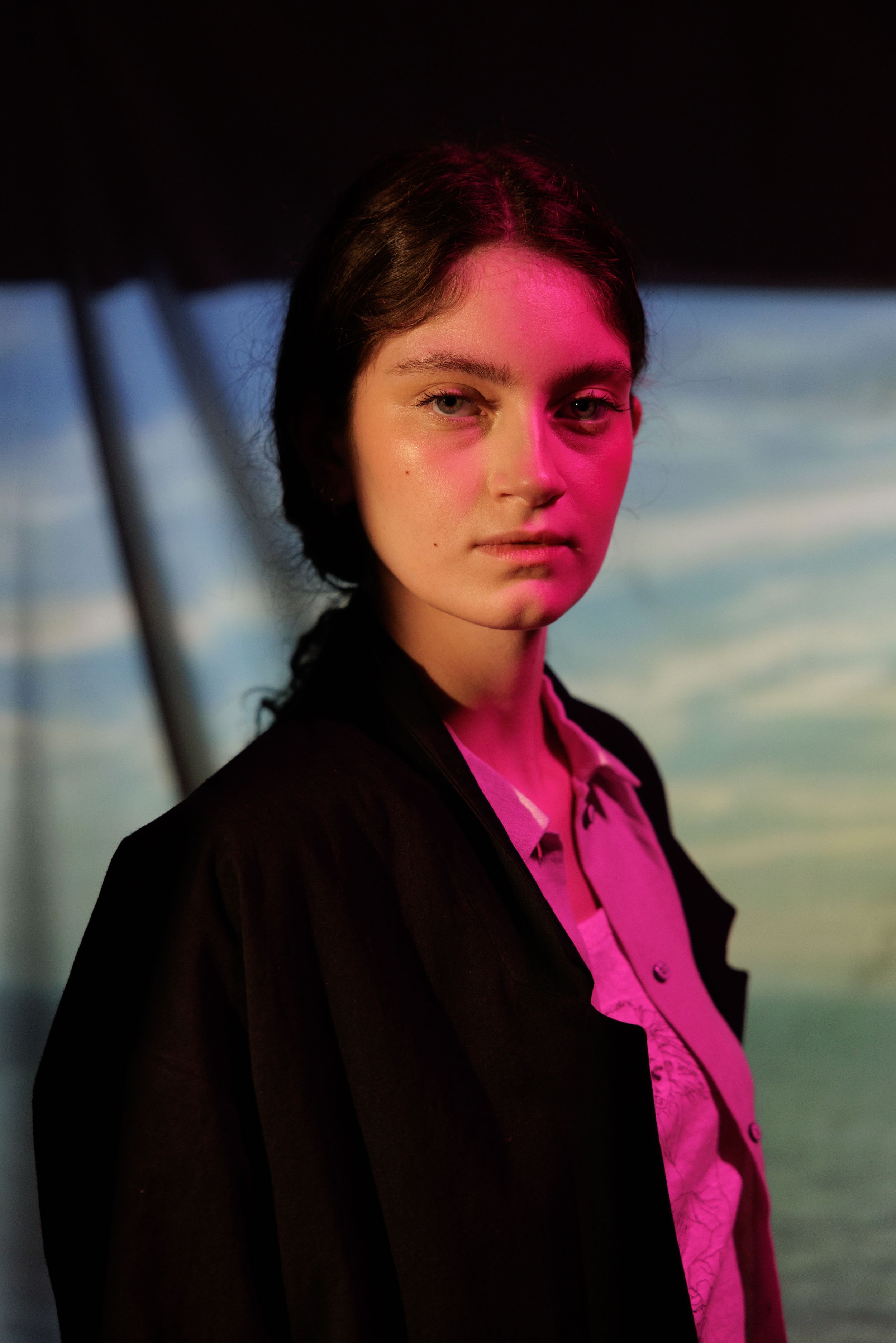Artistic portrait series lit with vibrant pink side lighting creating a cinematic effect against a sunset sky.