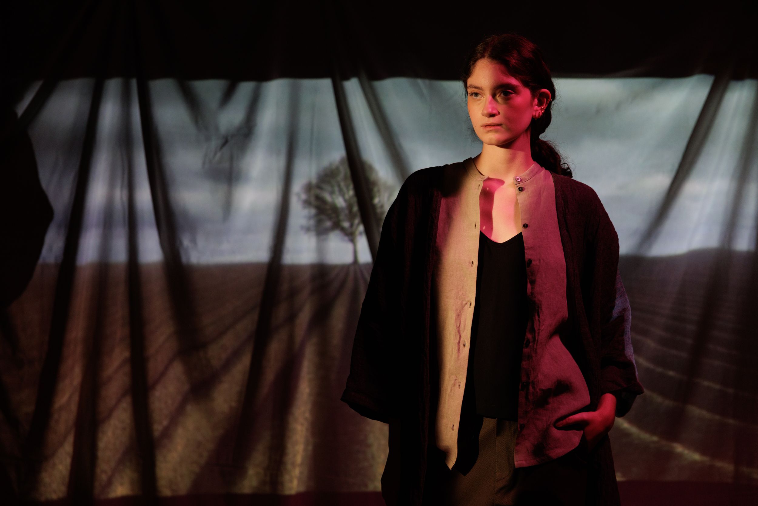 Dramatic low-angle shot of a person in dark clothing against a shadowy background with red lighting.