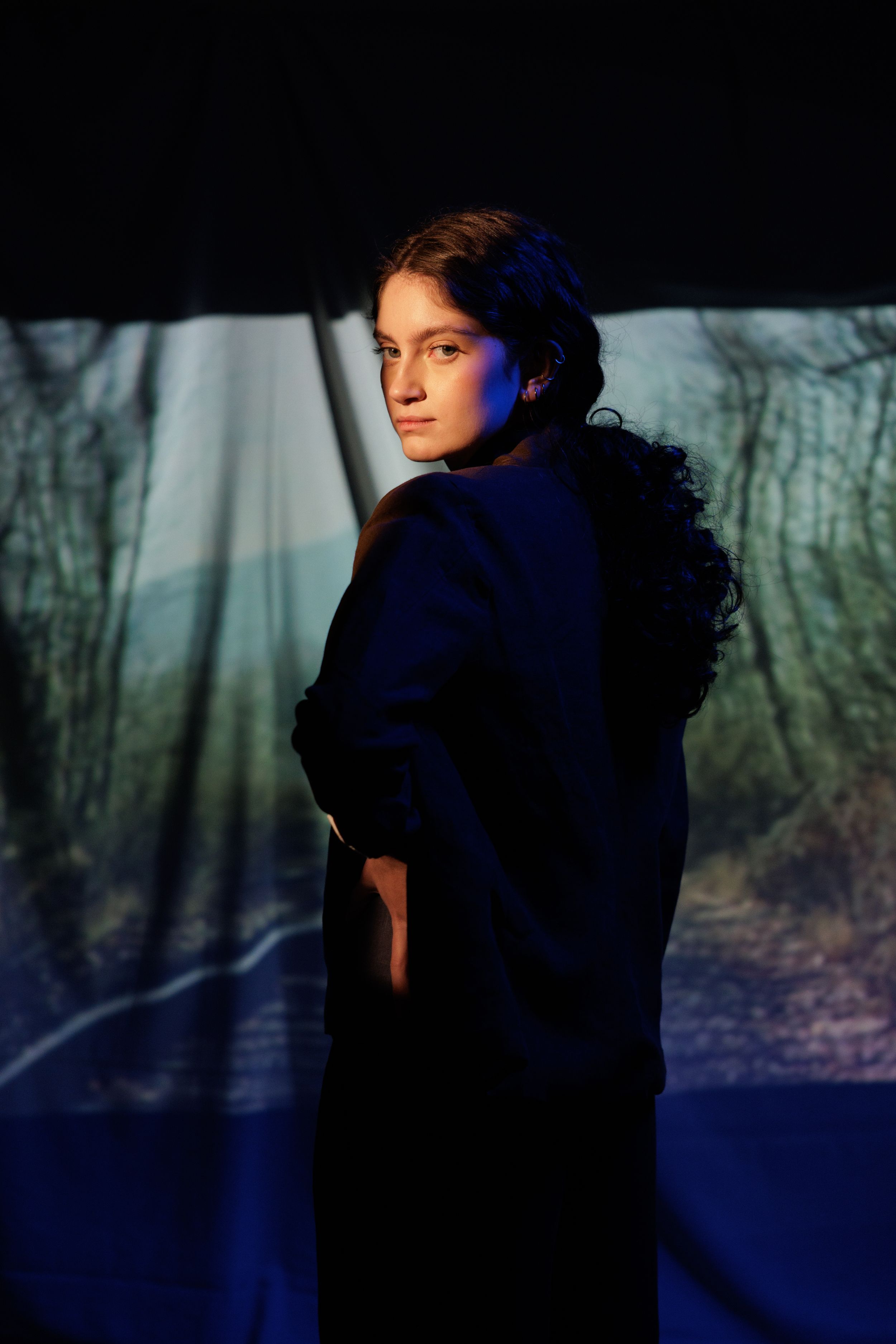 A silhouette of a person in a dark blue outfit stands against a moody forest background in a series of similar shots.