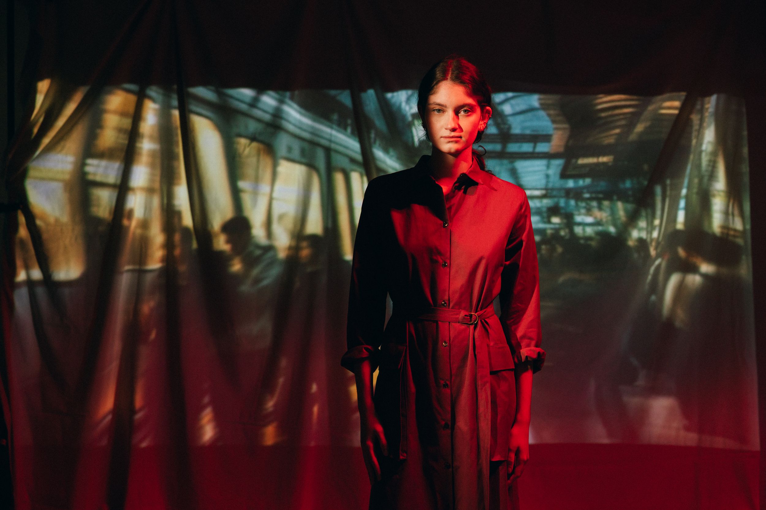 Person in red jacket stands in a dimly lit hallway with dramatic lighting and reflective surfaces.