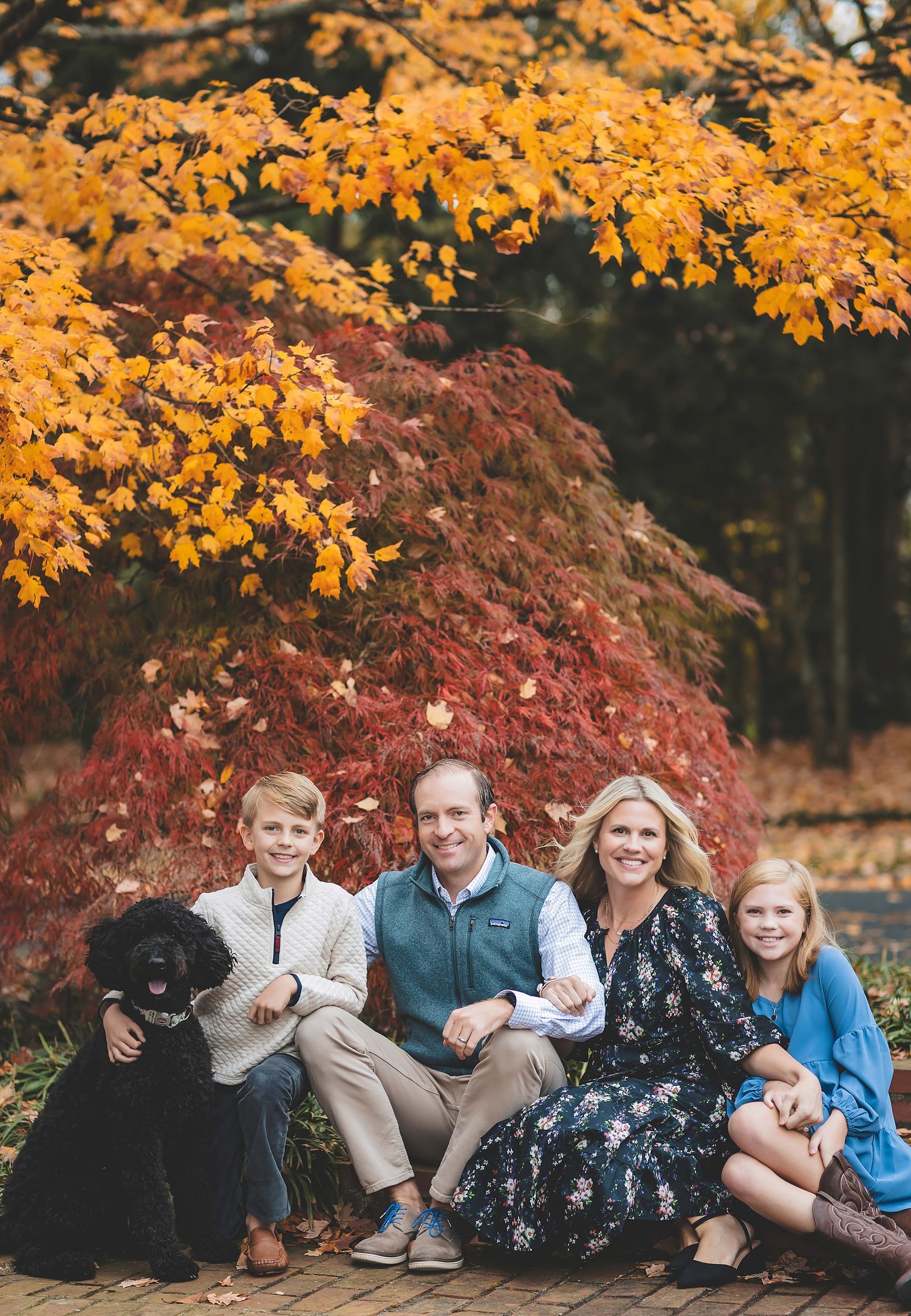 A group sits together outdoors against a backdrop of vibrant orange and burgundy autumn foliage.