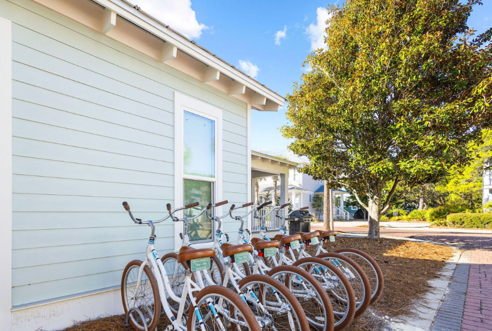 A row of parked rental bikes lined up against a white building on a sunny day.