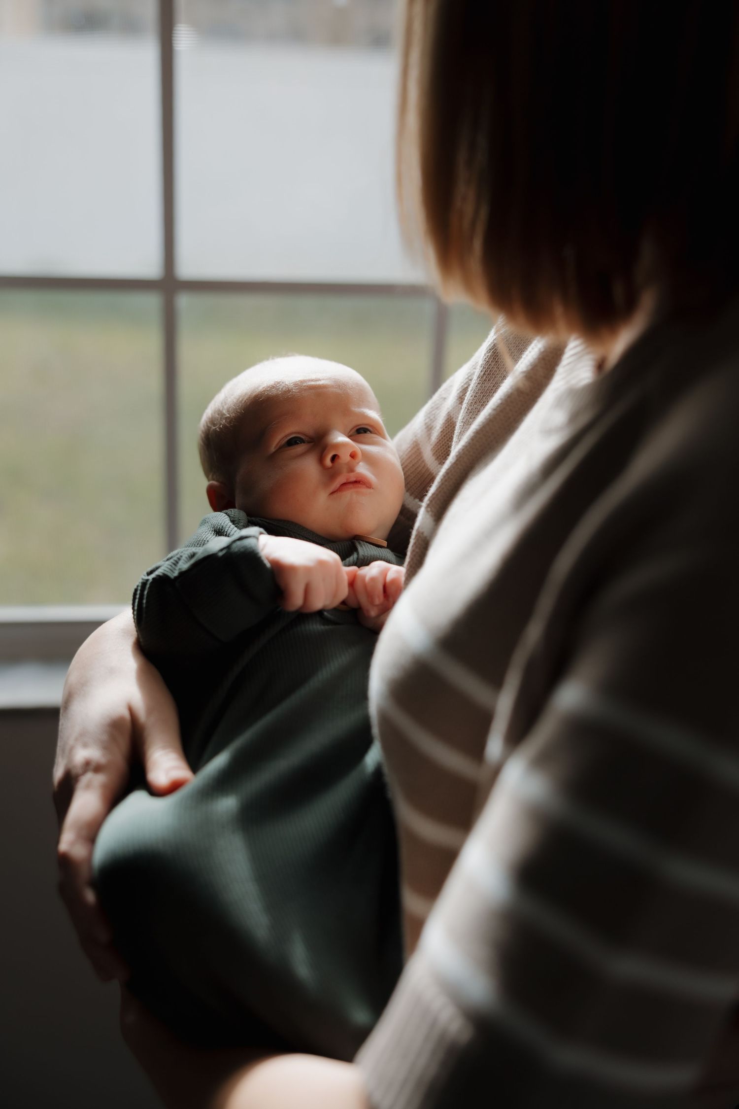 Baby rests peacefully against caregiver near window in soft natural light.