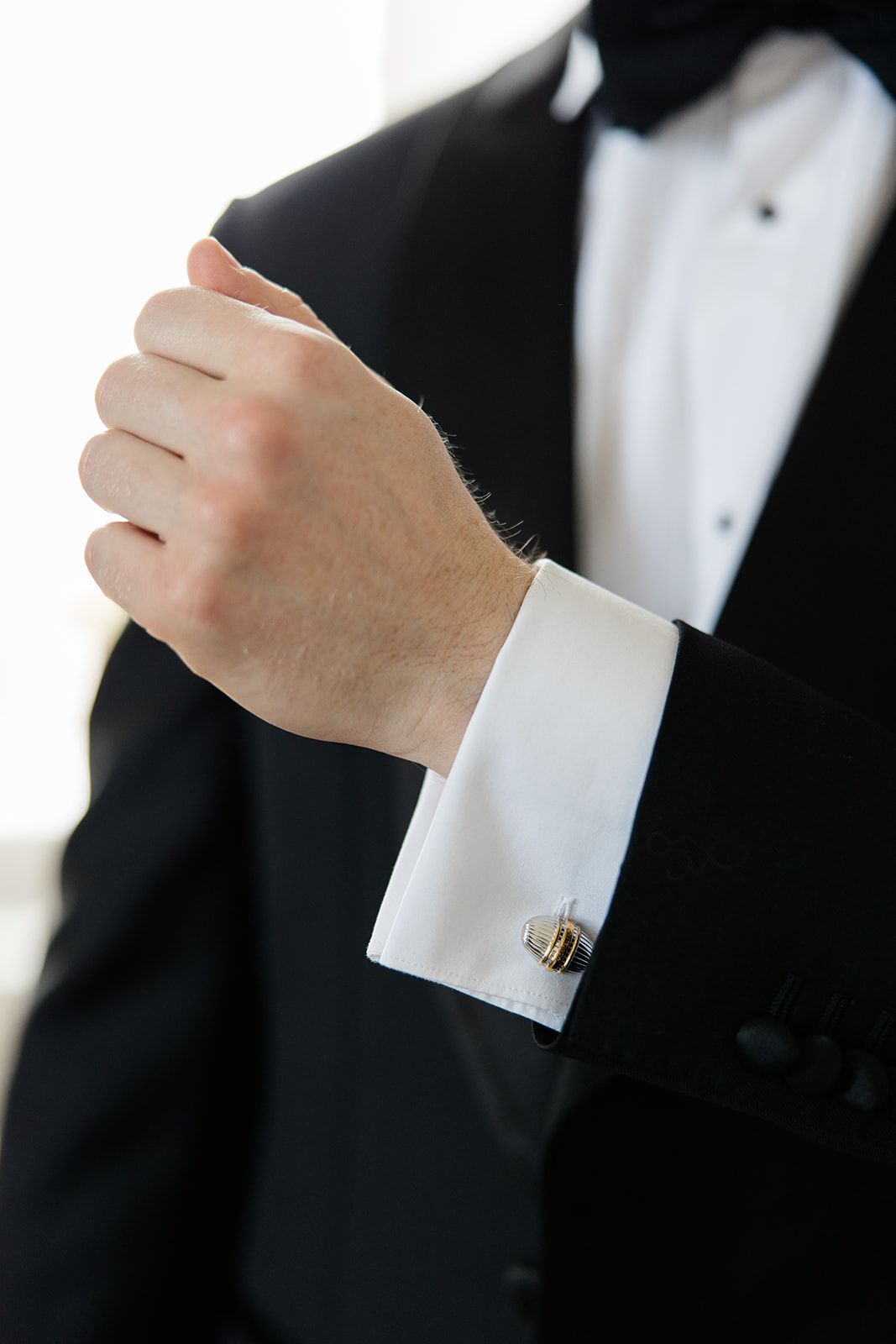 Close-up view of a formal tuxedo sleeve with white French cuff and gold cufflink showing elegant men's fashion detail.