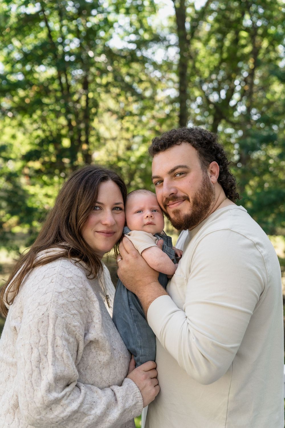 A loving family shares tender moments together in a sun-dappled outdoor setting in Macedonia, Ohio in-home newborn photo session