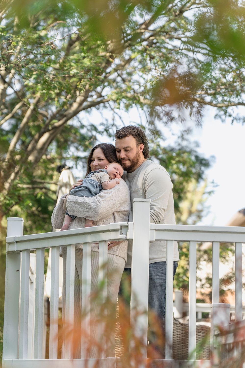 Two people share a tender embrace while leaning against a white wooden railing in Macedonia, Ohio in-home newborn photo session