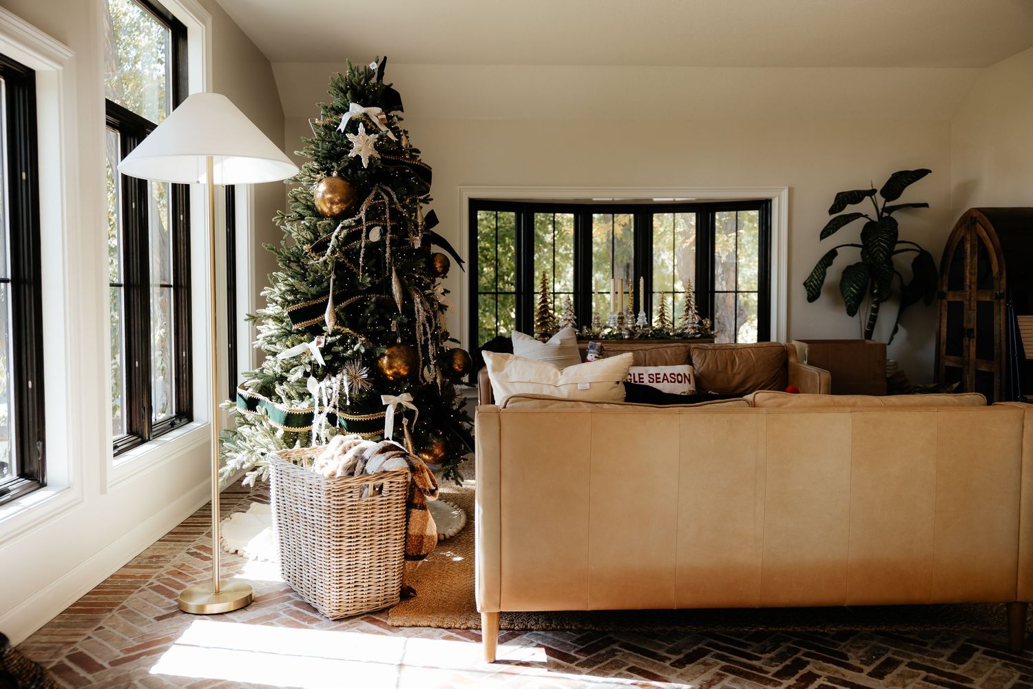 A decorated Christmas tree stands in a modern living room with large windows and a beige sofa.