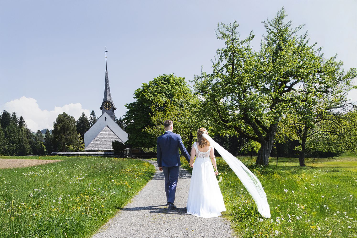 A couple walks along a scenic country path through blooming meadows and green fields on a sunny day.